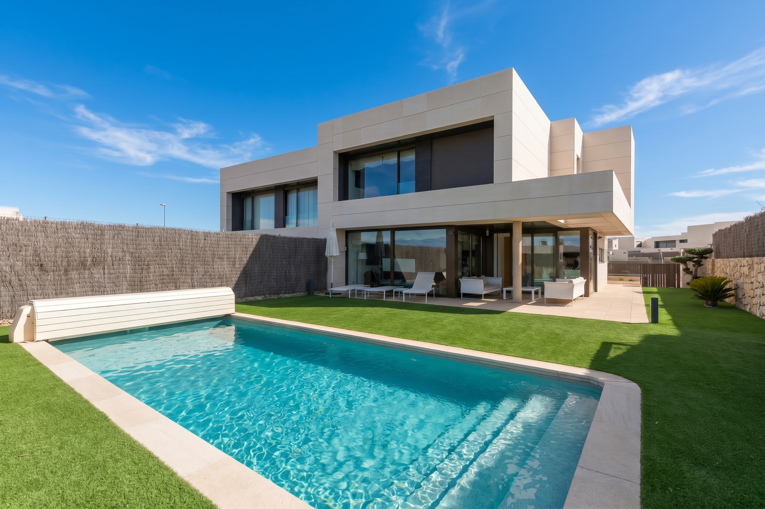 Modern two-story beige villa with a swimming pool, green lawn, and patio furniture under a clear blue sky. [AI-generated text] [AI-modified]