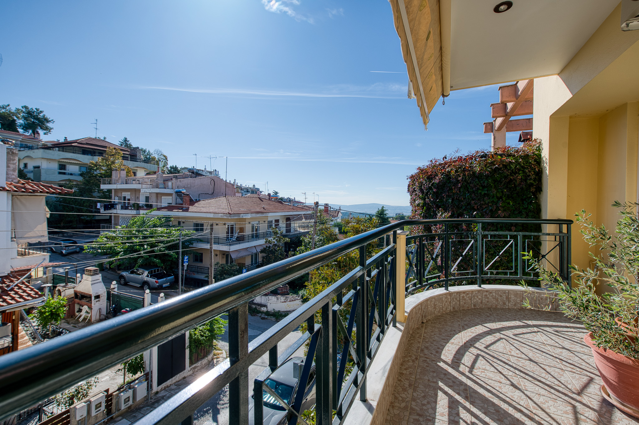 Sunny balcony with black metal railing, potted plant, and a view of a residential neighborhood under a clear blue sky. [AI-generated text]