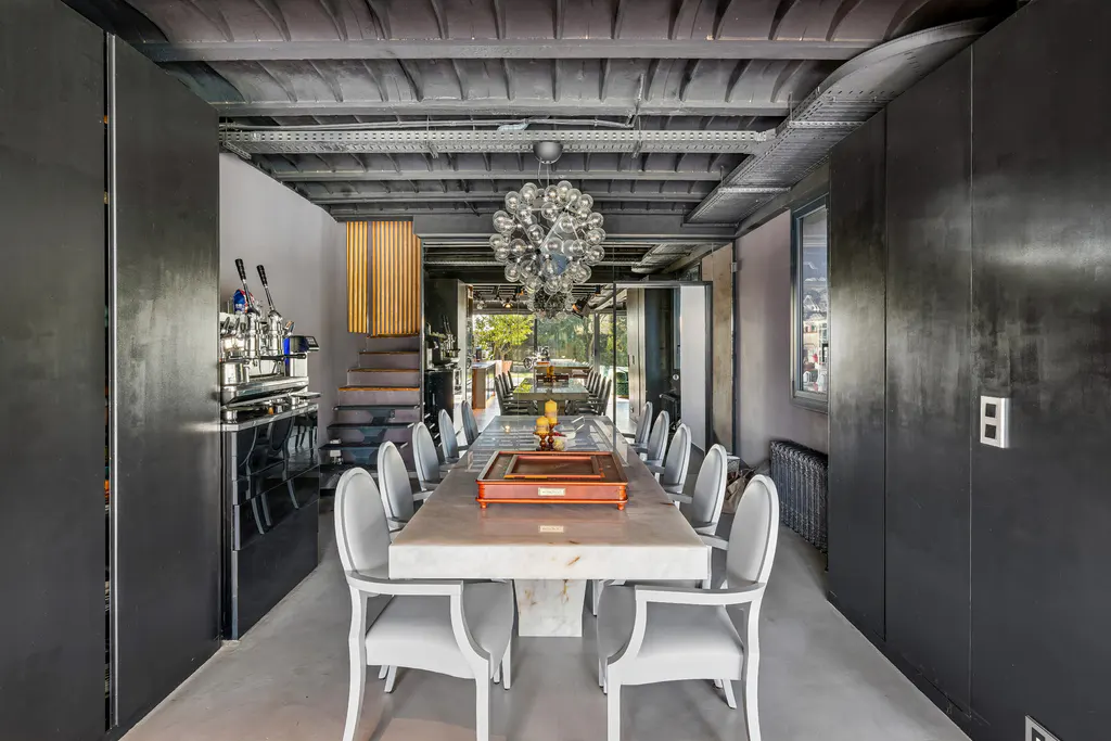 A modern dining room with a long marble table, white chairs, and a unique chandelier. Black walls and exposed ceiling add industrial charm.
