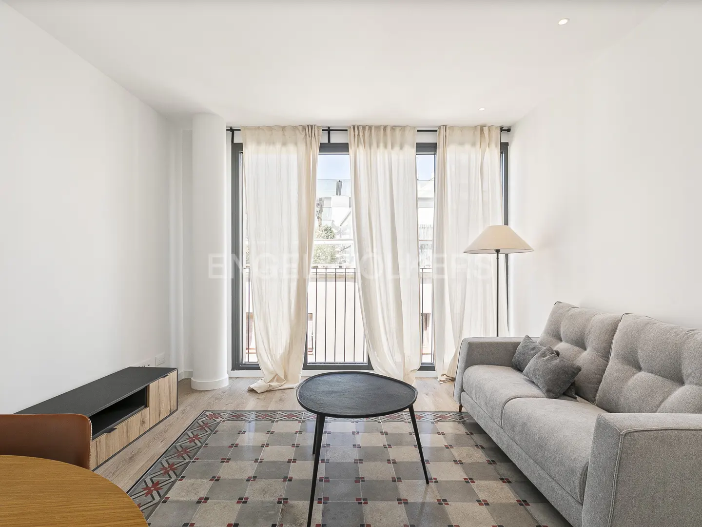 Bright living room with a gray sofa, black coffee table, and floor lamp near a window with sheer white curtains.