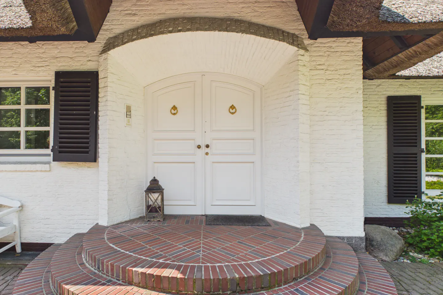 Front view of a white brick house with a thatched roof and a double white door with gold hardware.