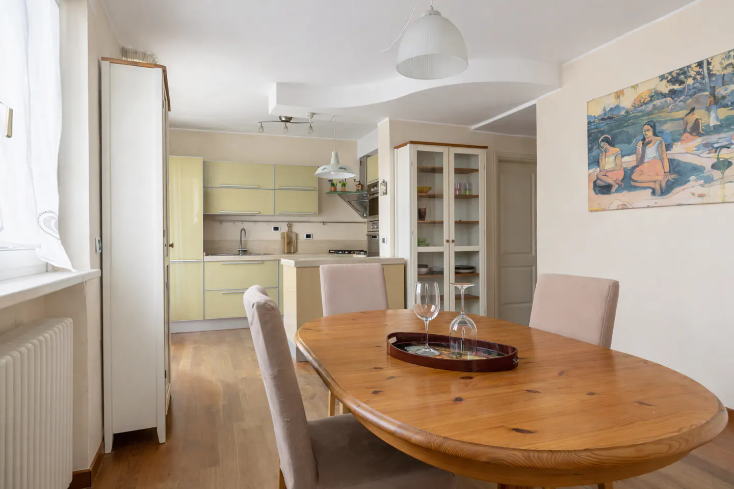 A bright kitchen and dining area with a wooden table, chairs, and a painting on the wall.