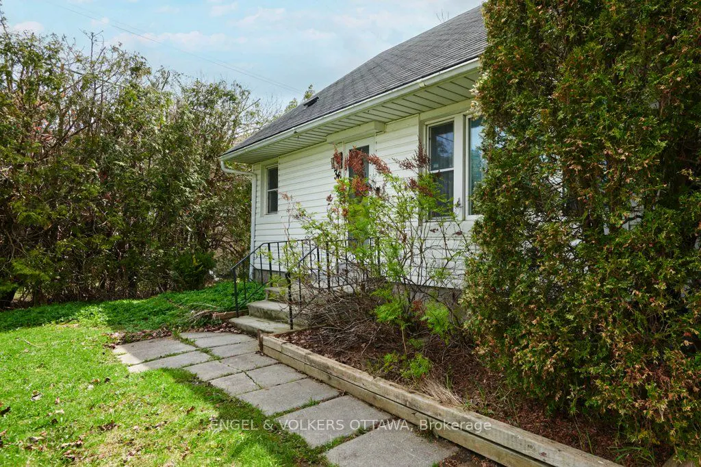 Exterior view of a white house with a gray roof, green bushes, and a stone walkway.