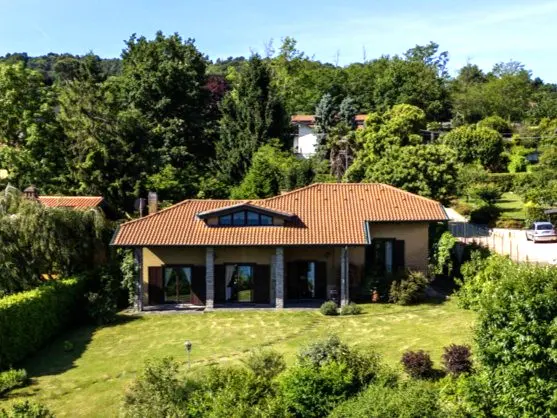 A tan house with a red tile roof sits on a green lawn surrounded by trees.