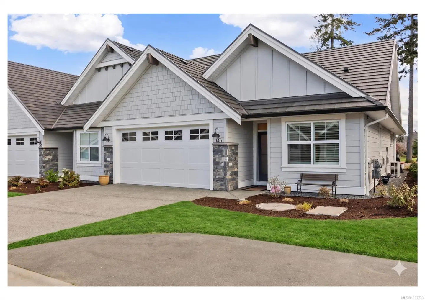 Exterior view of a light gray house with a white garage door, brown roof, and green lawn. A bench sits near the front door.
