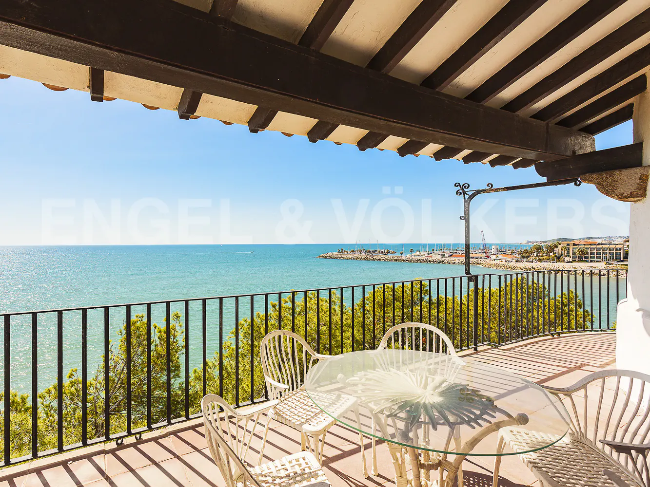 Balcony with a glass table and white chairs overlooking the ocean and harbor on a sunny day.