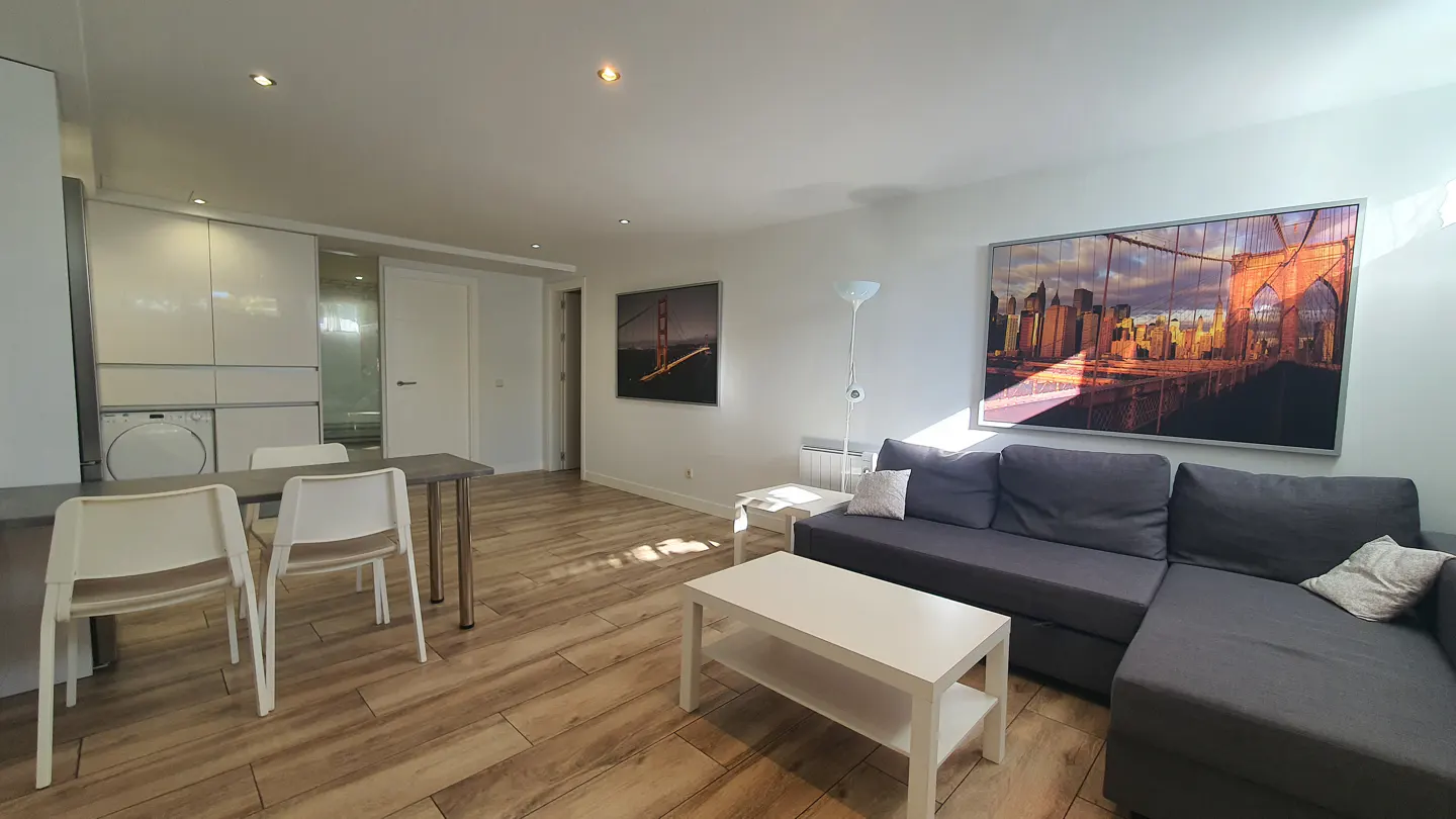 Modern living room with wood floors, grey sectional sofa, white coffee table, and large Brooklyn Bridge wall art.