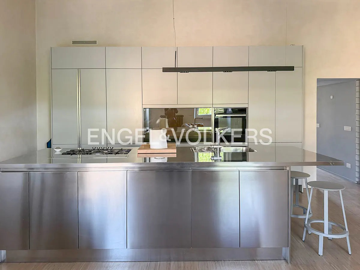 A modern kitchen with stainless steel island, cabinets, and countertops. Two stools are visible.