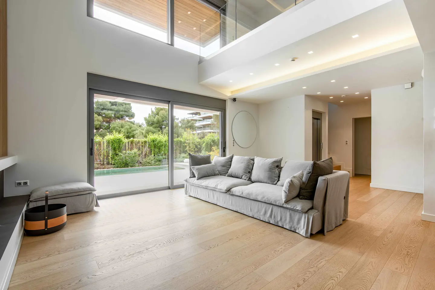 Bright living room with a gray sofa, wood floors, and large sliding glass doors to a green yard. High ceilings and modern design.