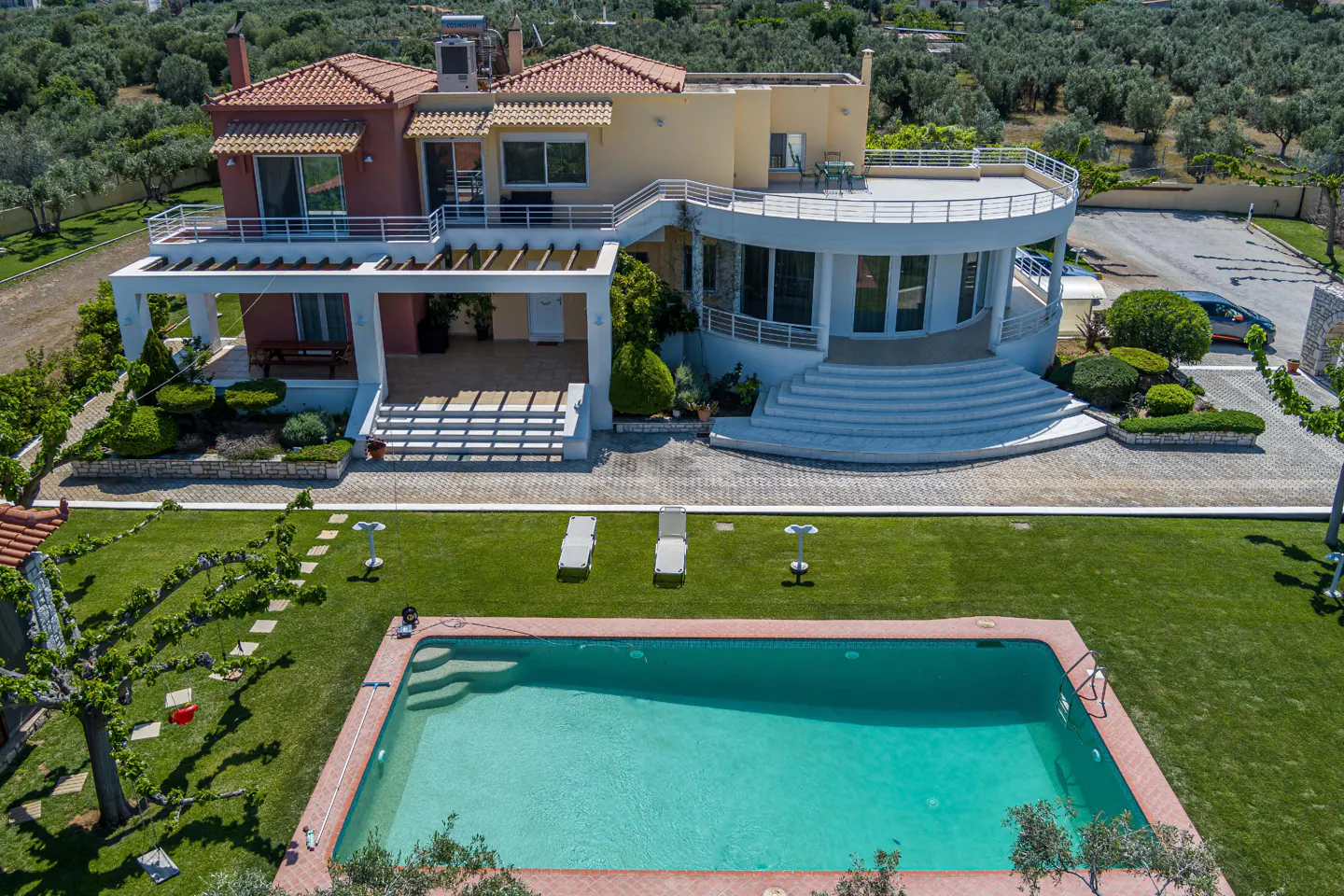 Aerial view of a two-story house with a red tile roof, a pool, and a green lawn.