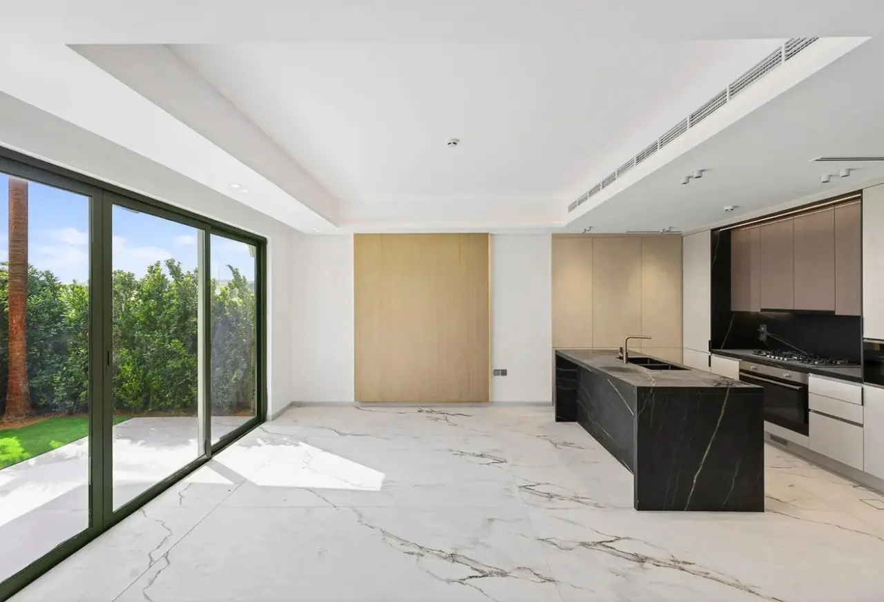 Bright, modern kitchen with marble floors, a black island, and floor-to-ceiling windows overlooking a green yard.