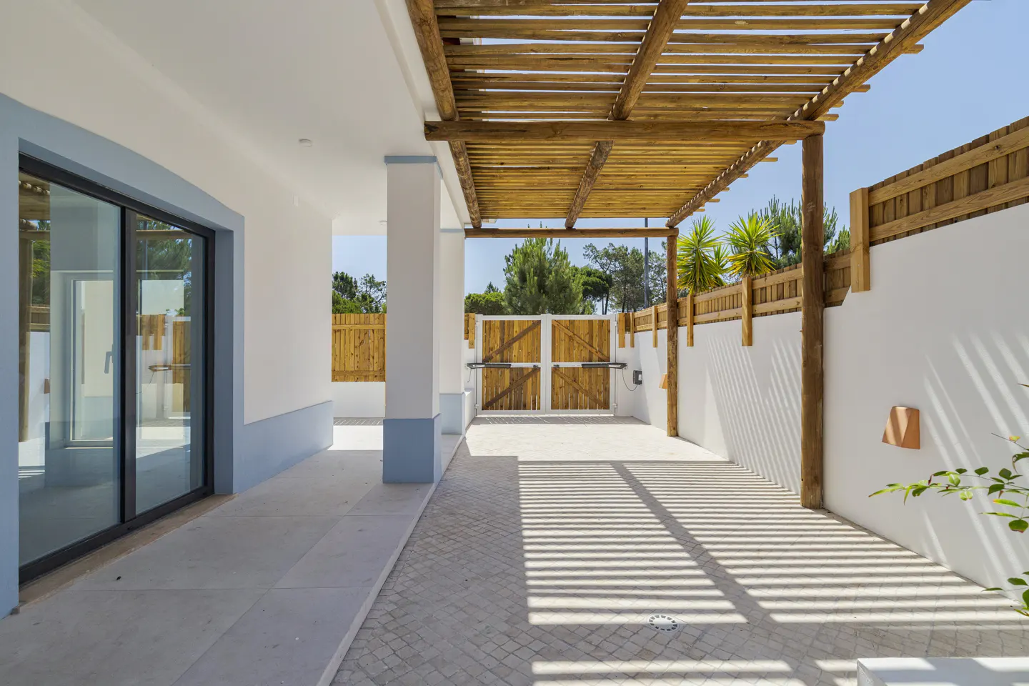 Patio with a wooden pergola, white walls, blue accents, and a wooden gate under a bright blue sky.
