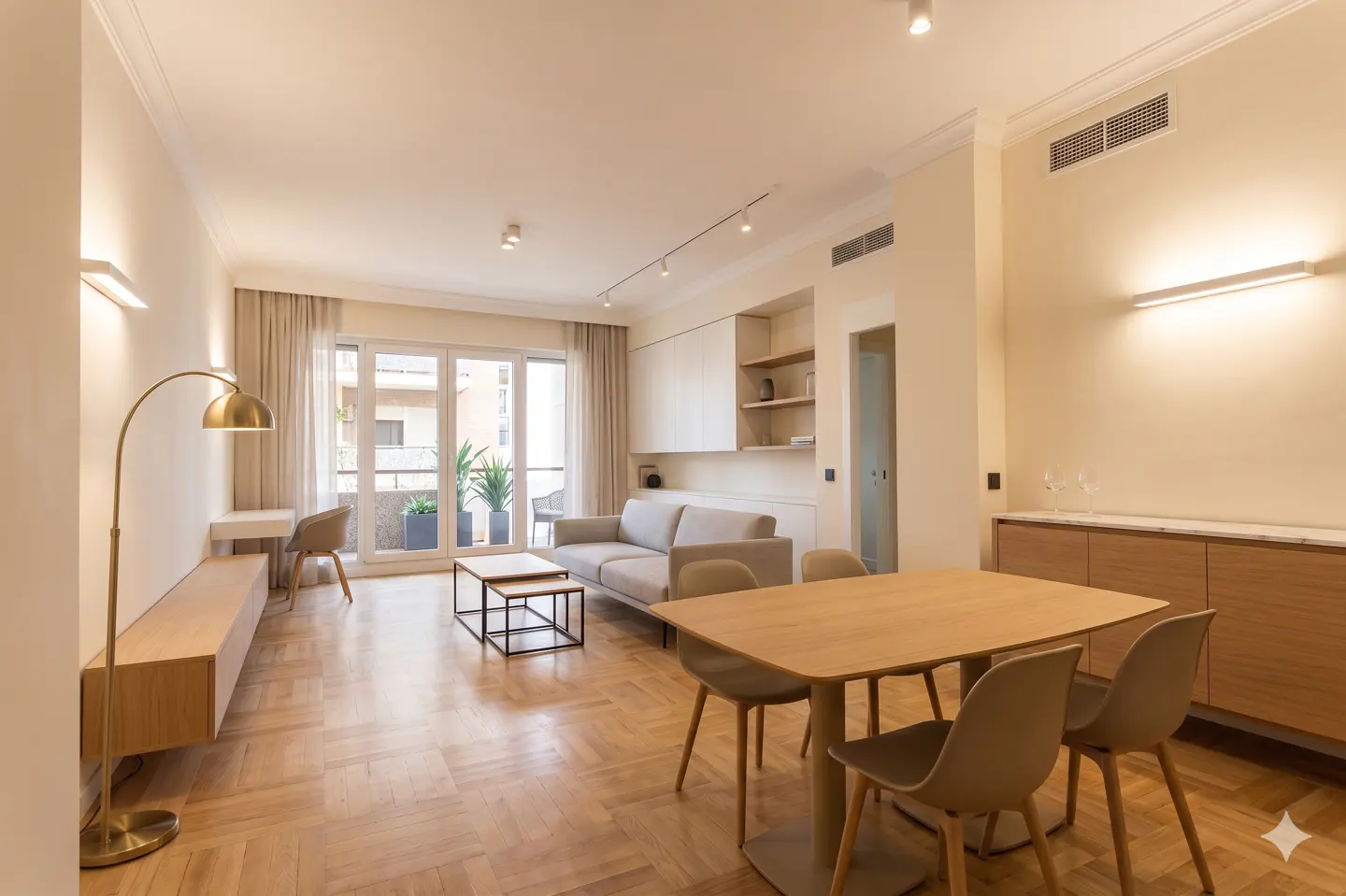 Bright, modern living room with wood floors, a dining table, sofa, desk, and balcony access. Neutral color palette.