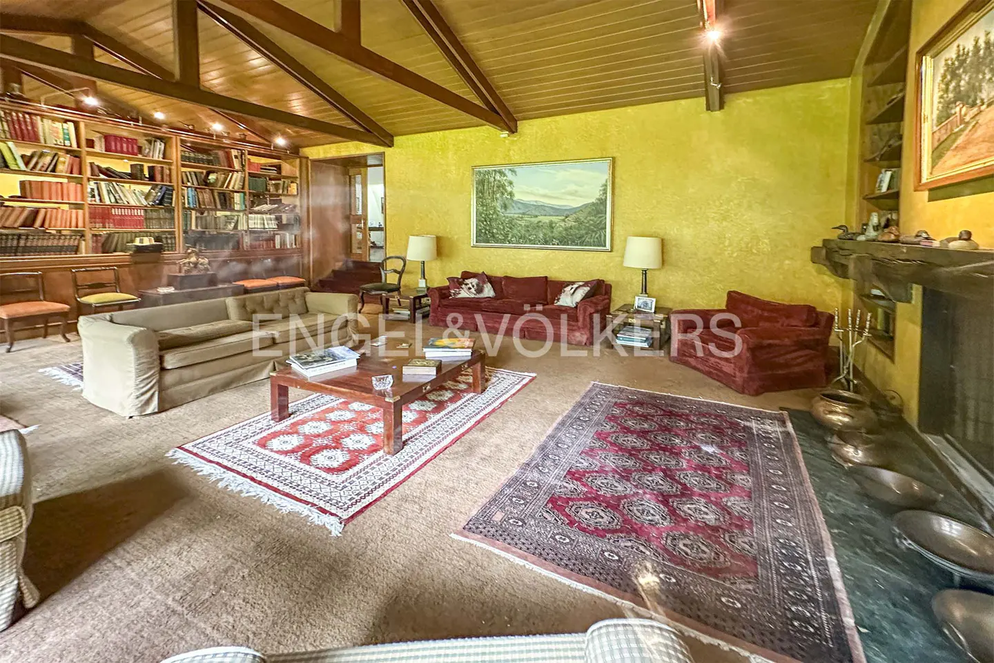 A living room with a fireplace, a red sofa, and a bookshelf filled with books. The walls are yellow.