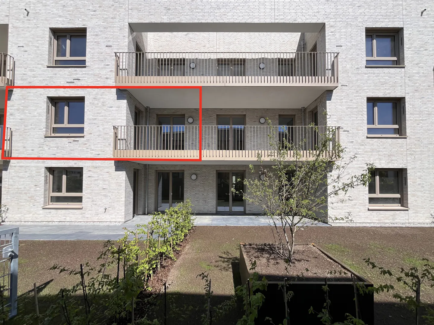 Exterior of a light brick apartment building with a balcony and a small garden.