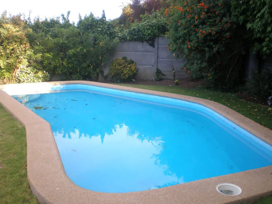 A bright blue swimming pool with a tan border, surrounded by green grass and lush greenery.