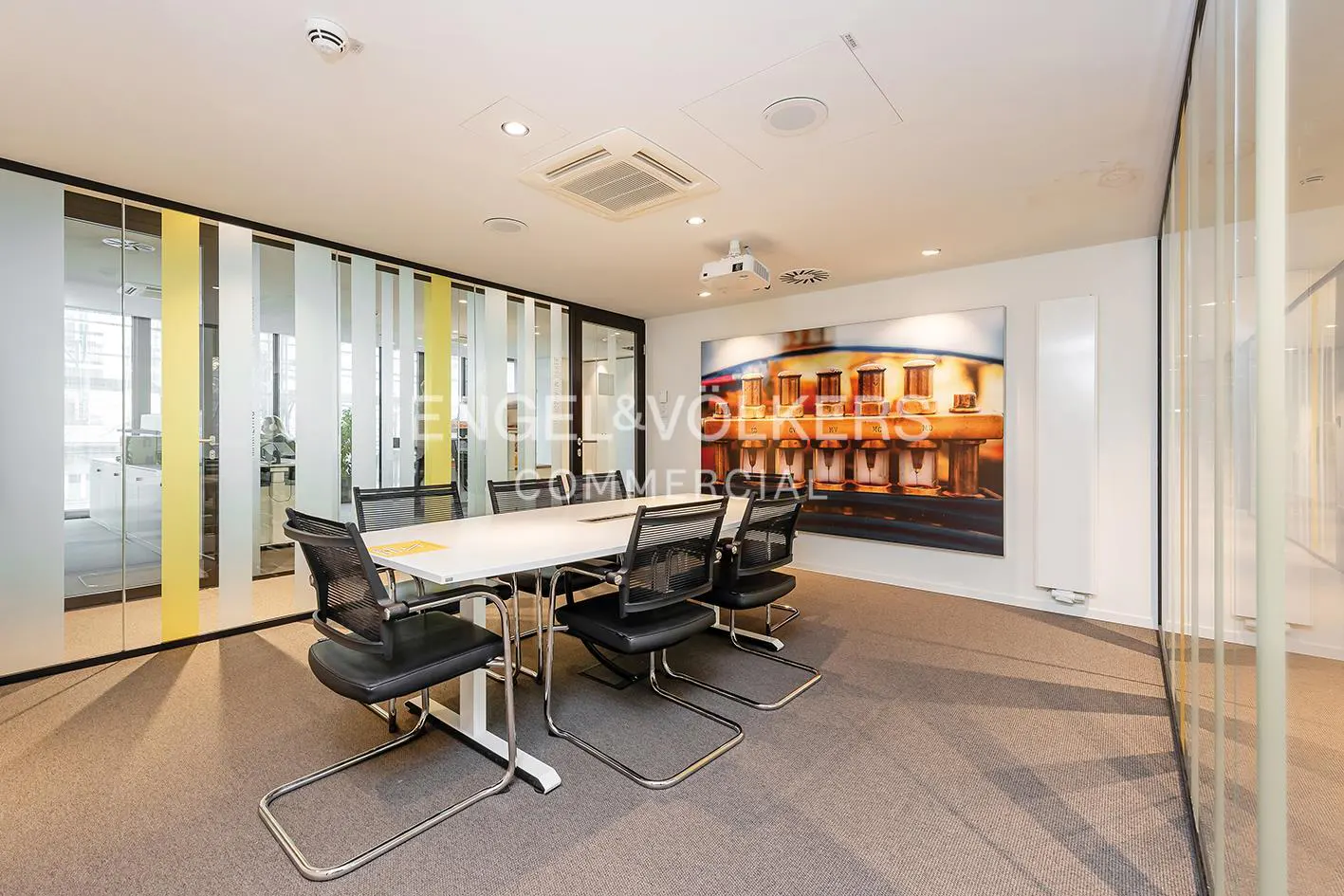 Bright office conference room with a white table, black chairs, and a large colorful painting on the wall.