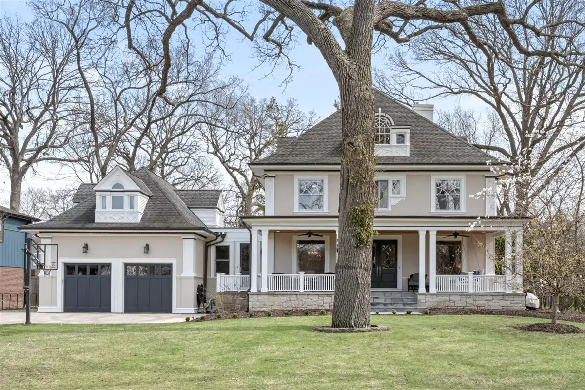 Beige two-story house with a gray roof, white porch columns, and a two-car garage on a green lawn.