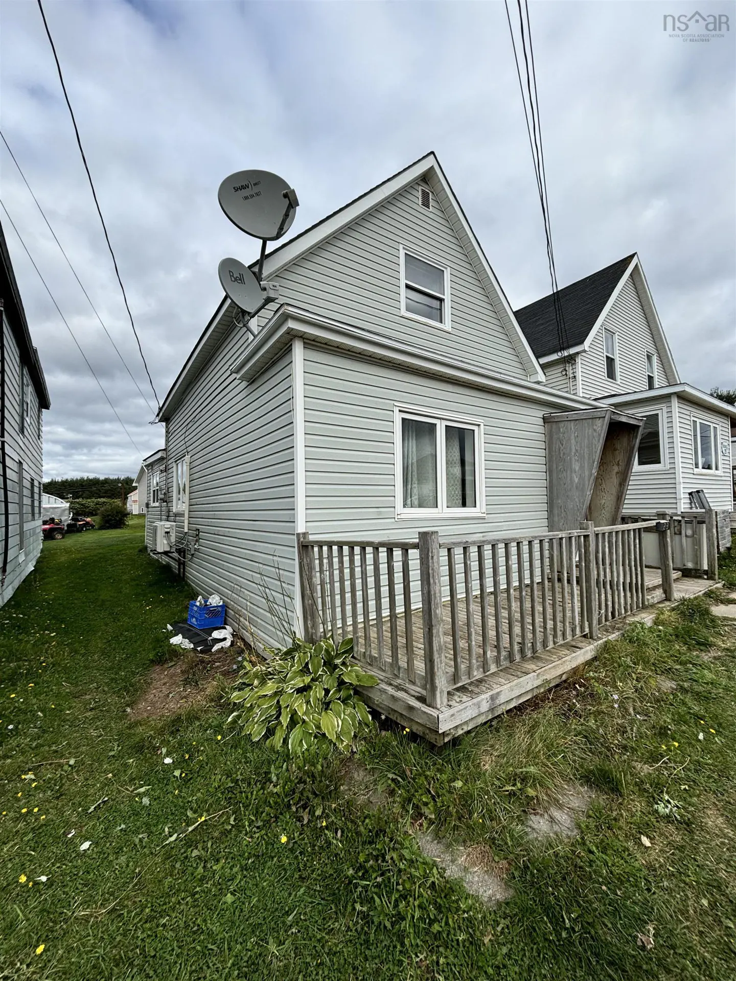 Exterior view of a light gray house with a wooden deck and two satellite dishes on the roof.