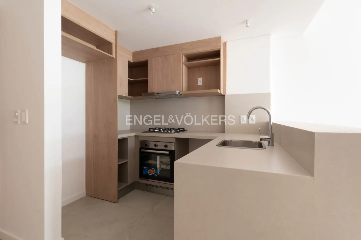 Modern kitchen with light wood cabinets, beige countertops, stainless steel oven, gas cooktop, and a sink.