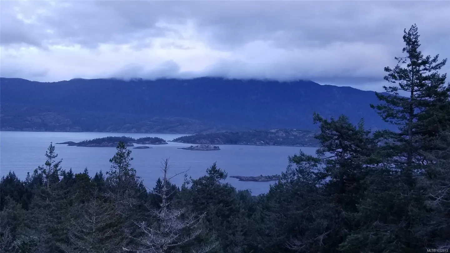 Overlook view of a lake with islands, mountains, and evergreen trees under a cloudy sky.