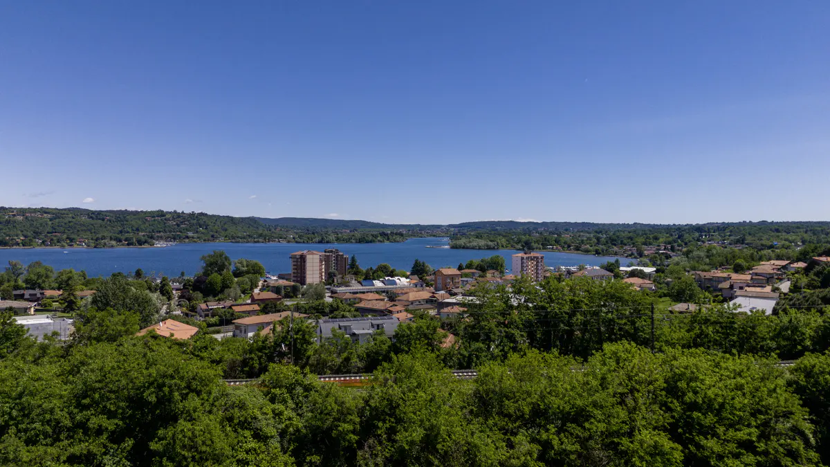 Scenic view of a blue lake surrounded by green hills and buildings with red roofs under a clear blue sky.