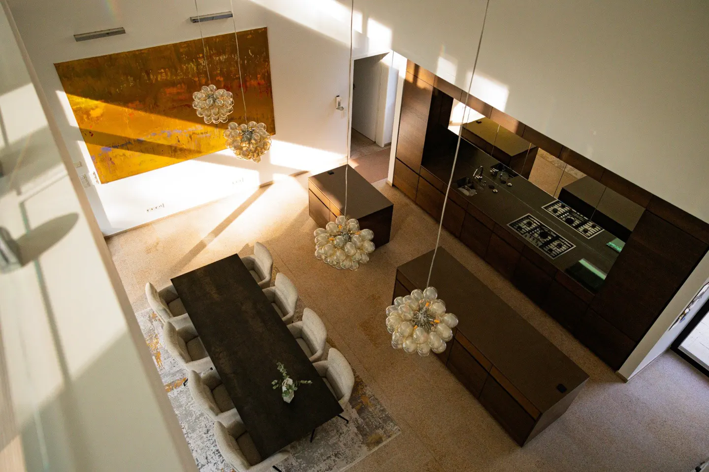 Overhead shot of a modern home interior with a dining table, kitchen island, and a large abstract painting. Chandelier lighting.