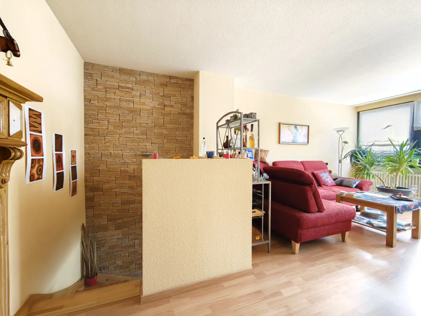 Living room with wood floors, a red sofa, and a stone accent wall. A metal shelving unit is behind a half wall.