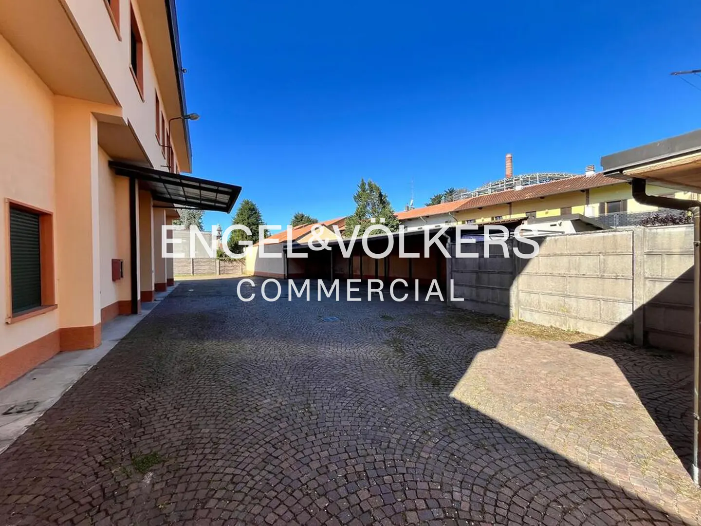 Exterior view of a commercial property with a cobblestone parking area and peach-colored building under a clear blue sky.