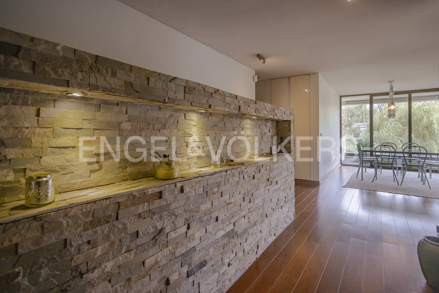 Interior view of a modern home with a stone accent wall, hardwood floors, and a dining area with large windows.