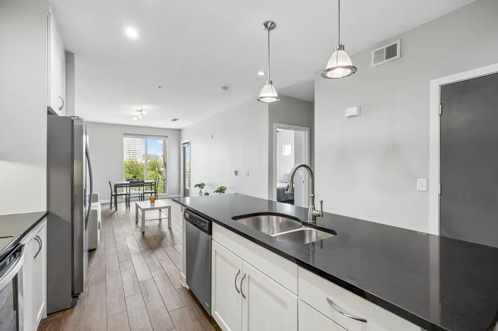A modern kitchen with white cabinets, black countertops, stainless steel appliances, and wood floors.