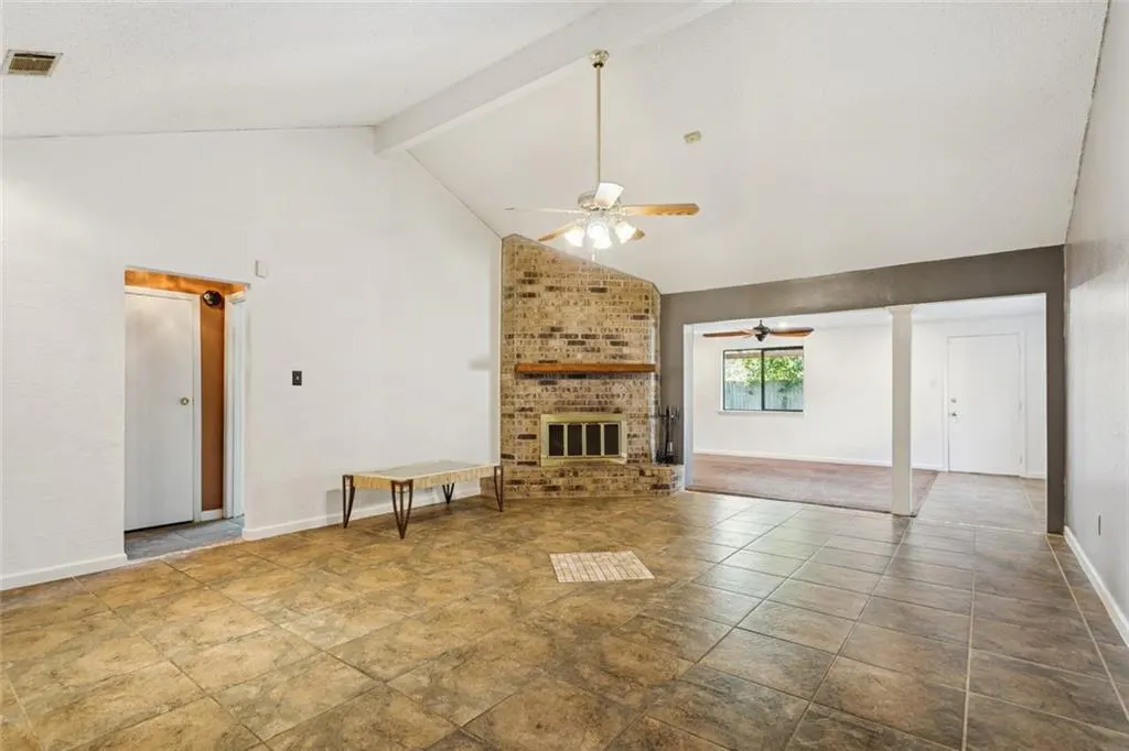A bright living room with a brick fireplace, tile floors, and a ceiling fan.