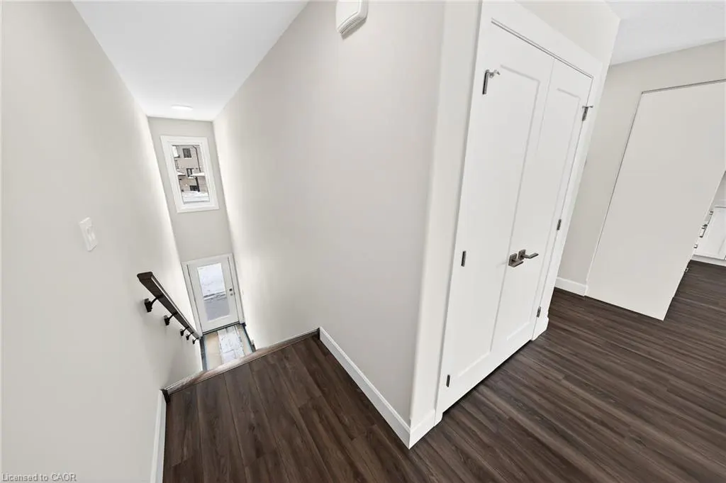 Interior view of a home featuring dark wood floors, white walls, and a staircase leading down to a glass door and window.