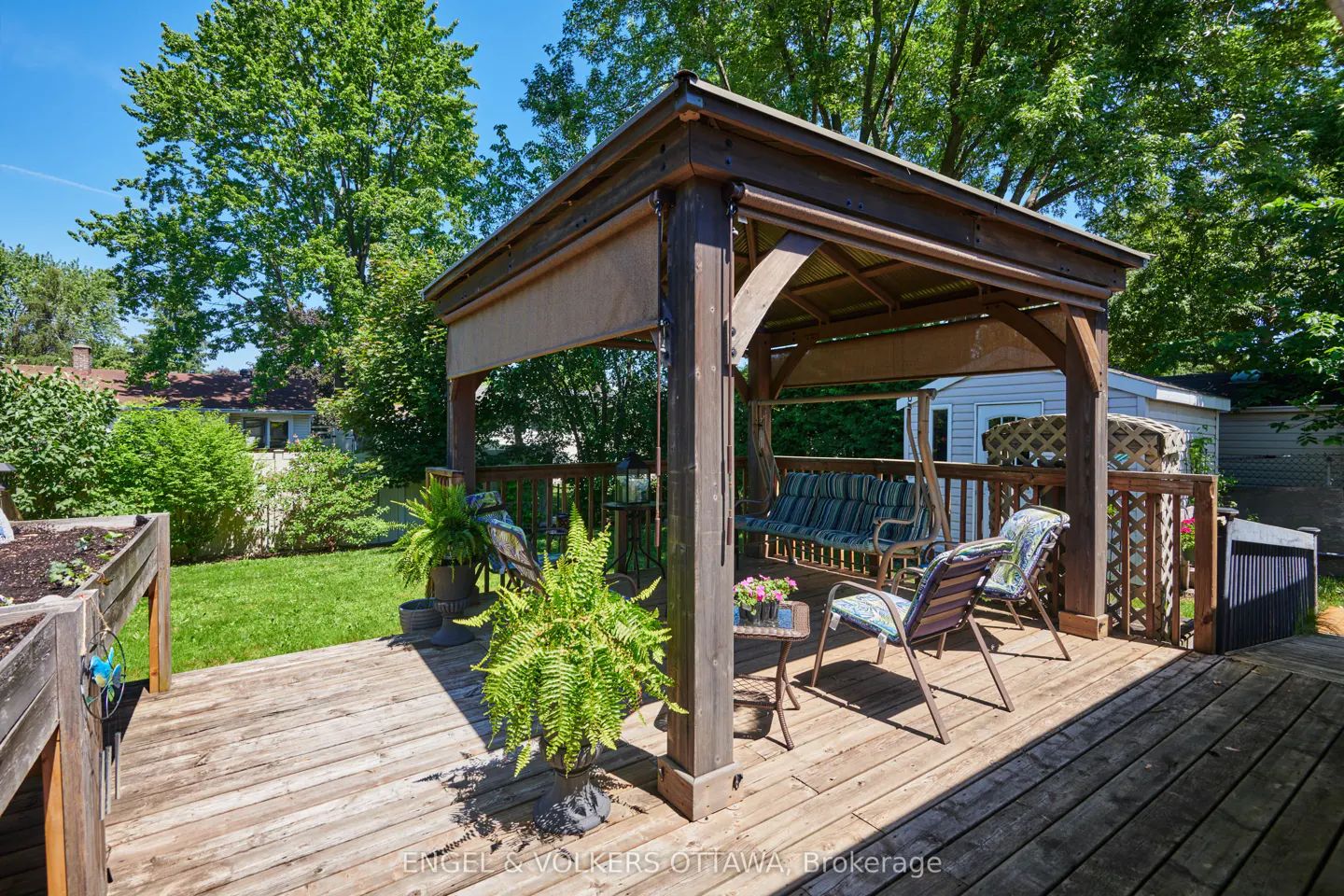 Wooden deck with a gazebo, patio furniture, and a lush green backyard on a sunny day.