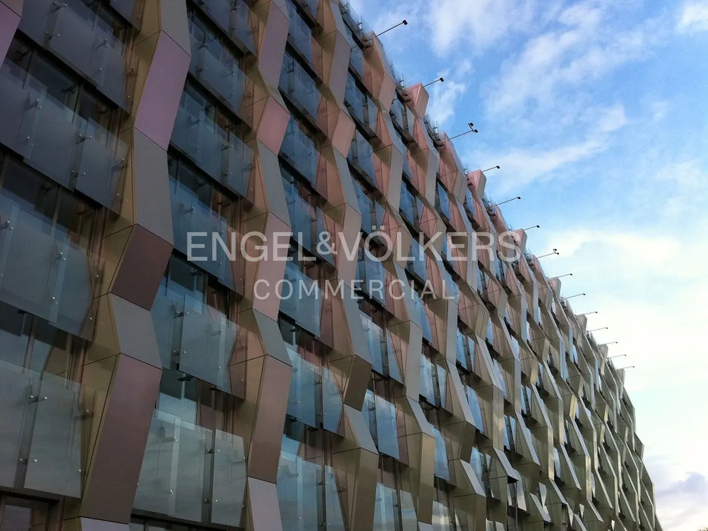 Modern building facade with a geometric, zig-zag pattern of metallic panels and glass windows against a blue sky.