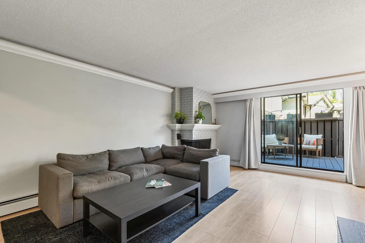 Living room with a grey sectional sofa, black coffee table, brick fireplace, and sliding doors leading to a patio.