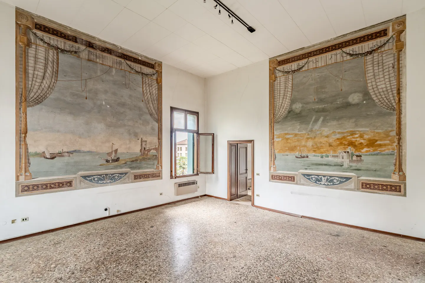 Empty room with terrazzo floor, white walls, and two large murals depicting seascapes with ships. A window and doorway are visible.