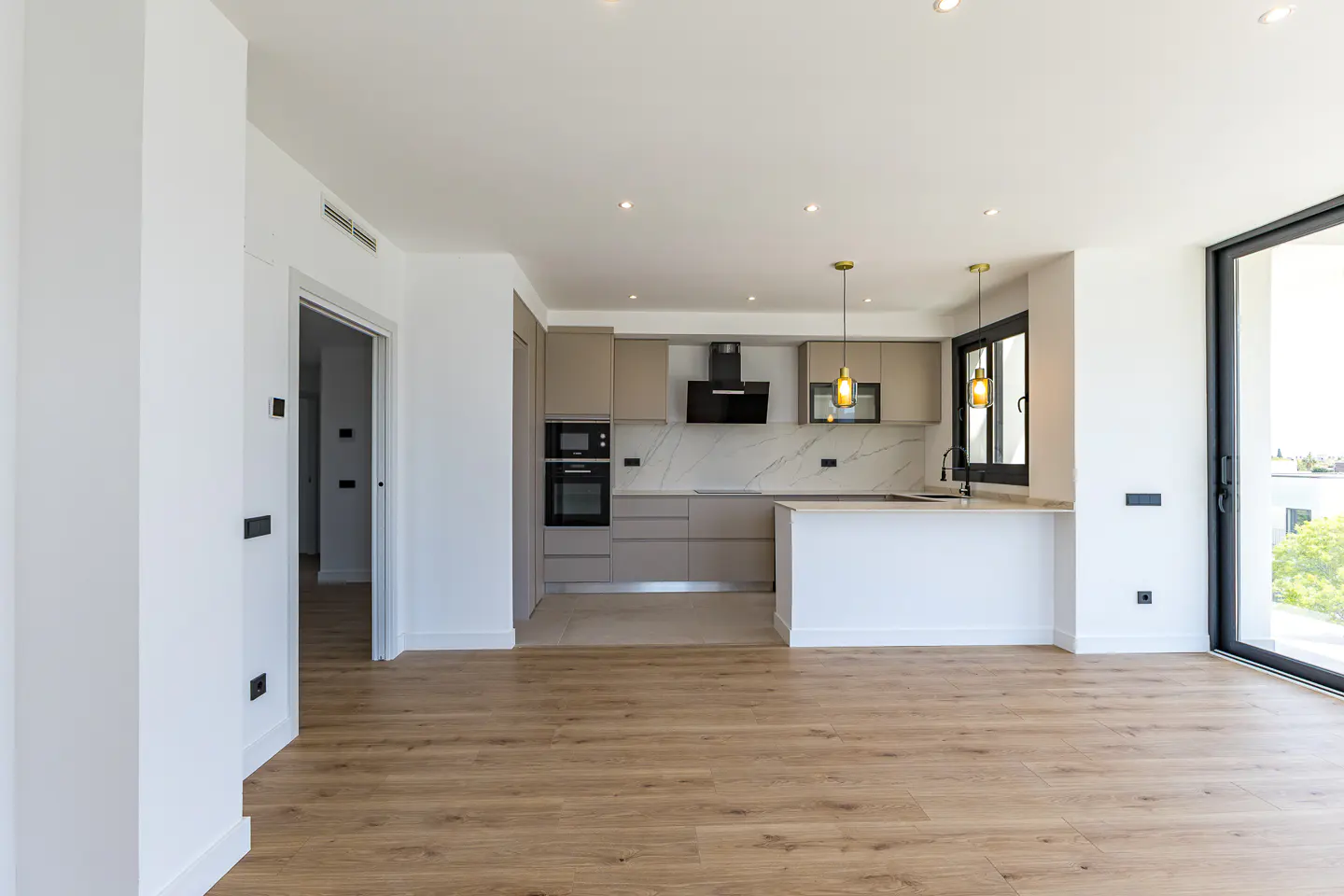 A bright, modern kitchen with wood floors, beige cabinets, a white island, and black appliances. A large sliding glass door lets in natural light.