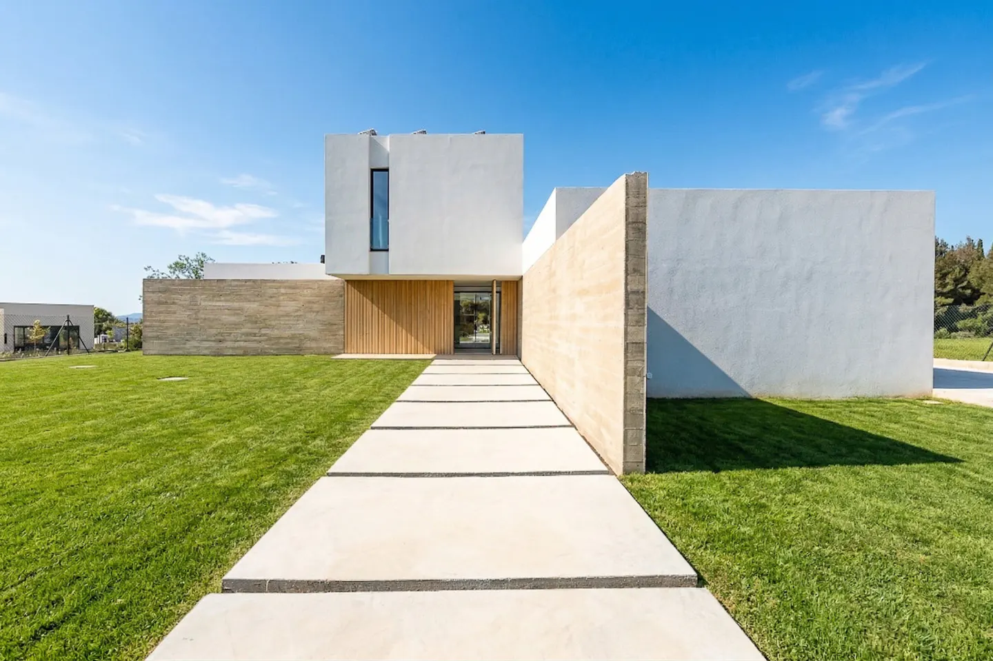 Modern white house with a concrete walkway leading to the front door, surrounded by green grass and a clear blue sky.