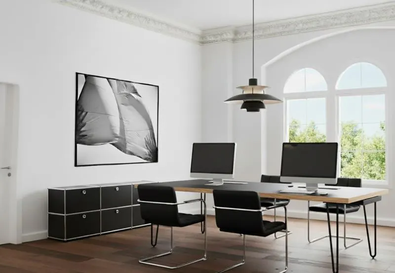 Bright office space with a long desk, black chairs, computers, and a black and white photo on the wall.