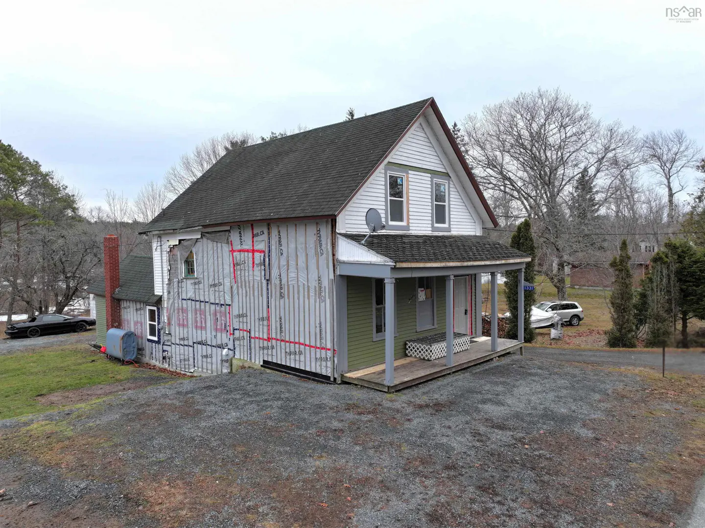 Exterior view of a two-story house with gray siding under construction, a green porch, and a gravel driveway.