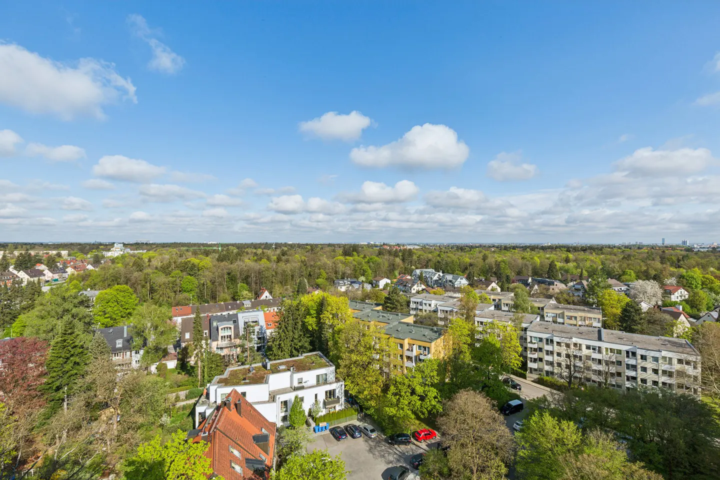 Aerial view of a residential area with houses, trees, and a blue sky with white clouds.