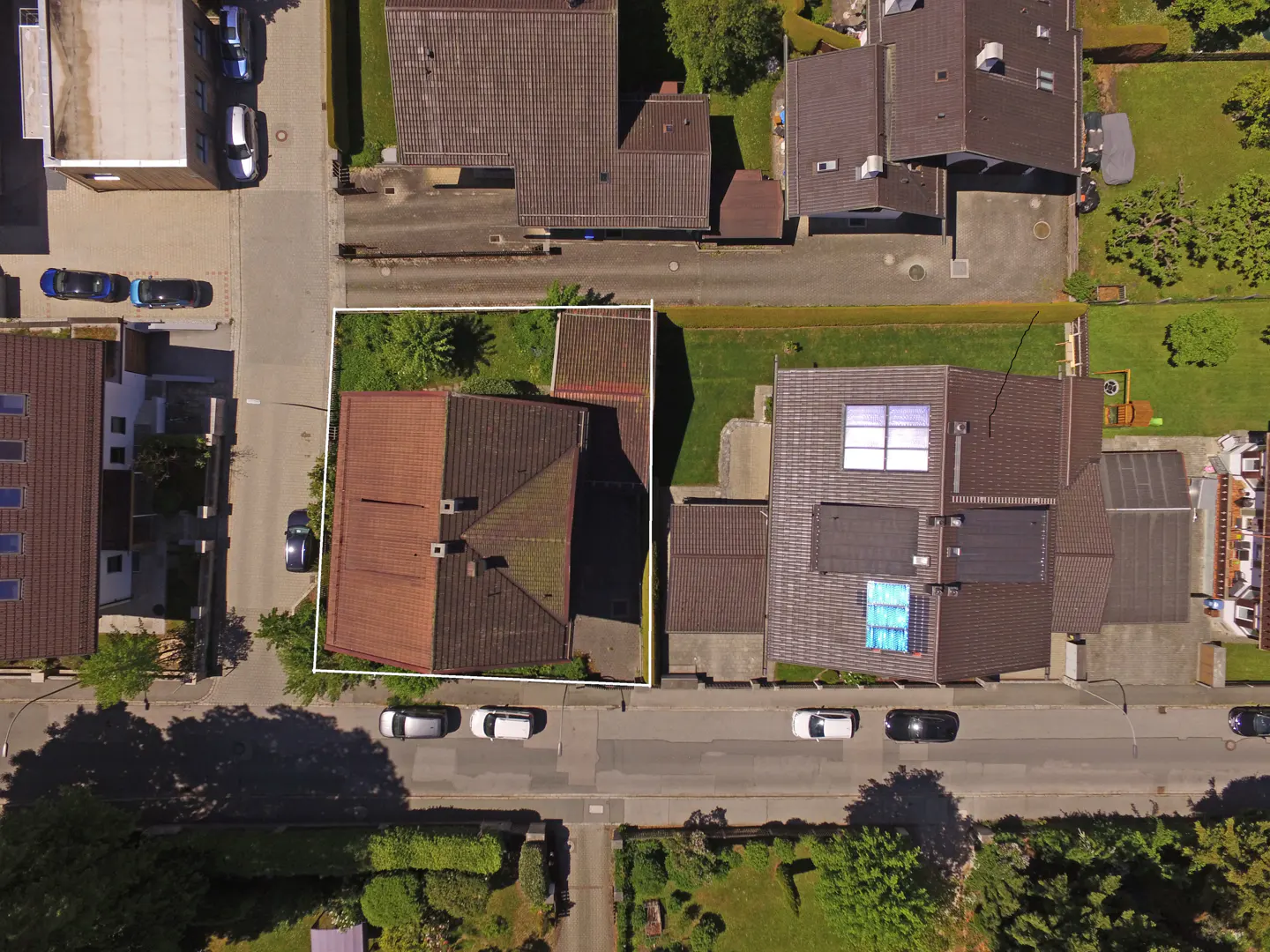 Aerial view of a house with a brown roof, outlined in white, surrounded by other houses, streets, and cars.