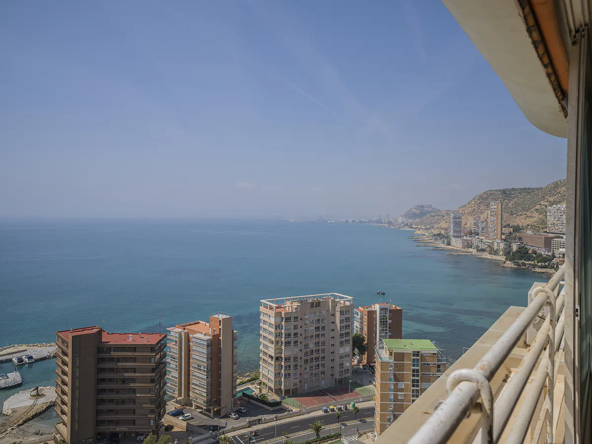 View from a balcony overlooking the ocean, buildings, and coastline on a sunny day.