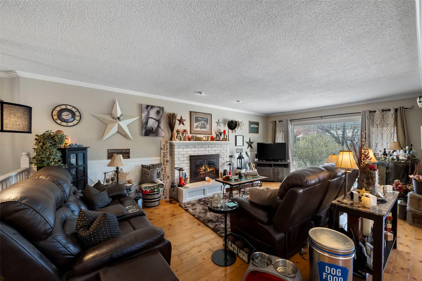Living room with brown leather sofas, a white brick fireplace with a fire, and wood floors. Western-themed decor adorns the walls.