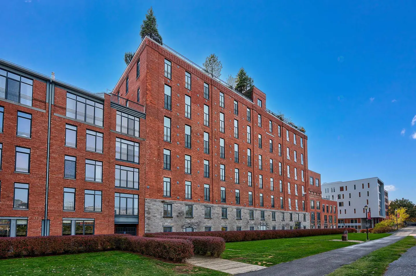 Exterior view of a red brick apartment building with black framed windows, green lawn, and blue sky.