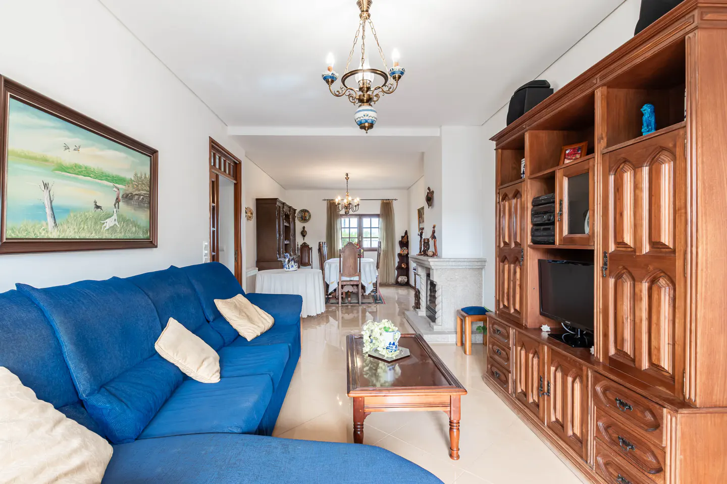 A living room with a blue sofa, a wooden TV cabinet, and a dining area in the background.