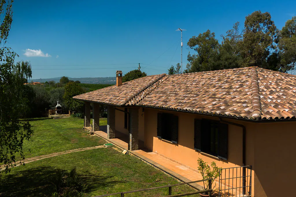 Exterior view of a one-story peach-colored house with a terracotta tile roof, a green lawn, and trees under a blue sky.