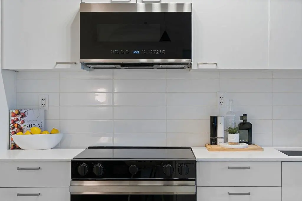 Modern kitchen with white cabinets, subway tile backsplash, and black oven and microwave. A bowl of lemons sits on the counter.