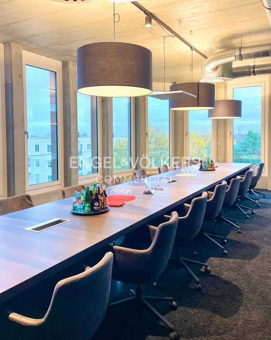 Conference room with a long wooden table, gray chairs, and large windows overlooking a cityscape.